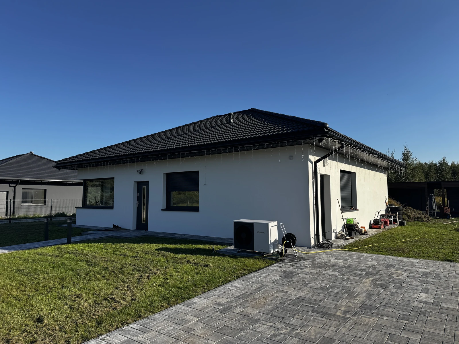 Front i boczna elewacja jasnego domu z ciemnym dachem, stolarką i ułożoną kostką brukową